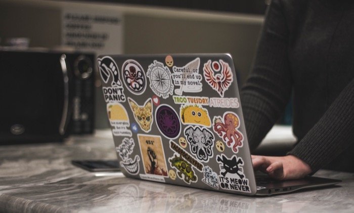 An unprofessionally-stickered laptop, in front of an unprofessional microwave. Photo by NeONBRAND on Unsplash.